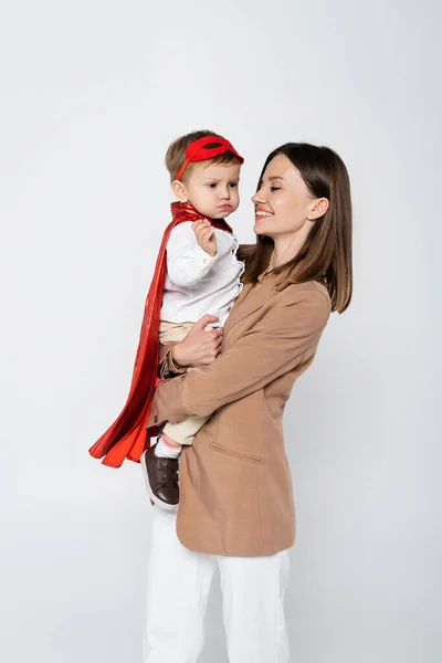 Happy Mother Holding Toddler Son Superhero Costume Isolated Grey — Fotografia de Stock