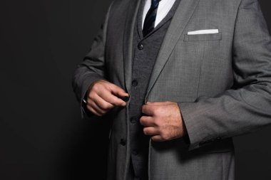 cropped view of businessman buttoning blazer on dark grey background
