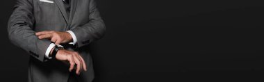 cropped view of man in suit checking time on wristwatch isolated on dark grey, banner