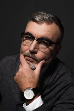portrait of serious senior man in eyeglasses and wristwatch looking at camera isolated on dark grey