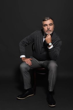 full length view of senior bearded man in stylish clothes sitting on dark grey