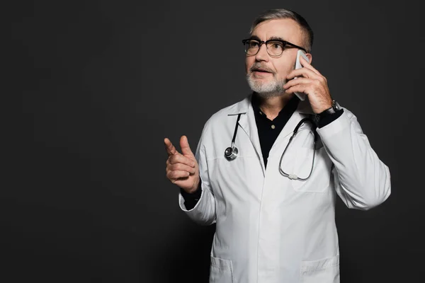 Bearded Doctor Looking Away Pointing Finger While Talking Cellphone Dark — Zdjęcie stockowe