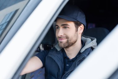 Smiling courier in uniform sitting in blurred car 