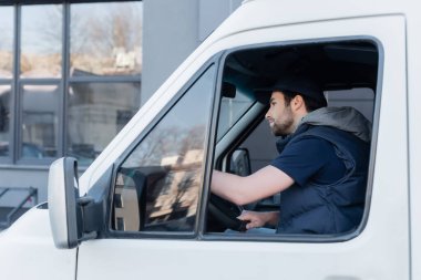 Side view of young courier in uniform driving auto 