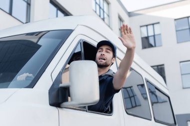 Worried courier waving hand while driving auto 