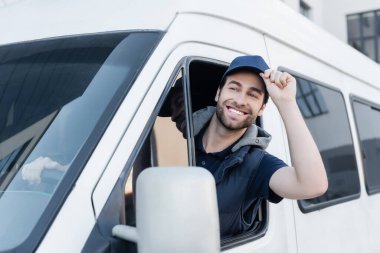 Smiling courier holding cap while driving auto 