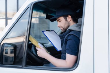 Side view of courier holding clipboard and parcel in car 