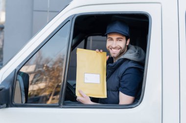 Smiling courier holding parcel and looking at camera in car 