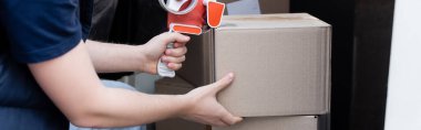 Cropped view of delivery man holding adhesive tape near cardboard boxes in car, banner 