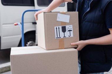 Cropped view of courier taking carton box from cart outdoors 