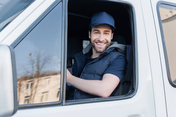 Positive courier in cap looking at camera in auto 