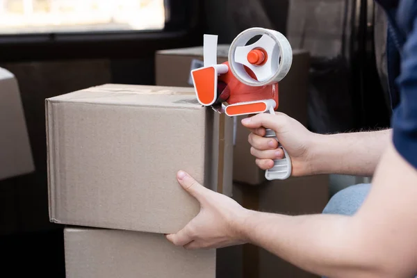 Cropped view of courier holding adhesive tape near box in auto