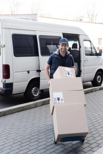 Smiling Courier Cap Holding Cart Boxes Car Outdoors — ストック写真