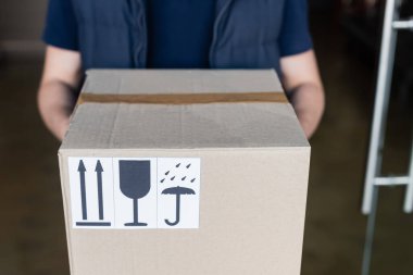 Cropped view of courier holding carton box with signs in hallway 