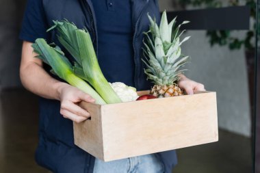Cropped view of courier holding wooden box with fresh food in hallway 