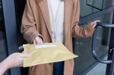 Cropped view of courier holding parcel near blurred woman and building outdoors 