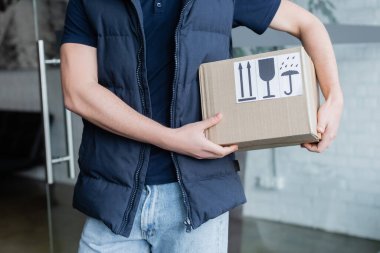 Cropped view of delivery man holding package with symbols in hallway 