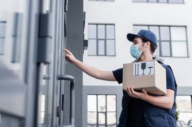 Low angle view of courier in medical mask holding package with signs near door of building outdoors   clipart