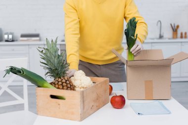Cropped view of man in latex gloves taking fresh food near boxes and rags in kitchen 