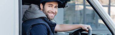 Positive delivery man smiling at camera while driving auto, banner 