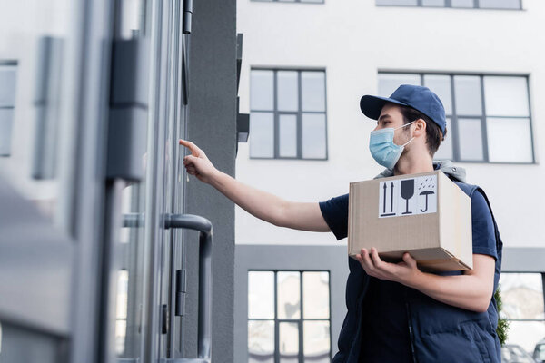 Low angle view of courier in medical mask holding package with signs near door of building outdoors  