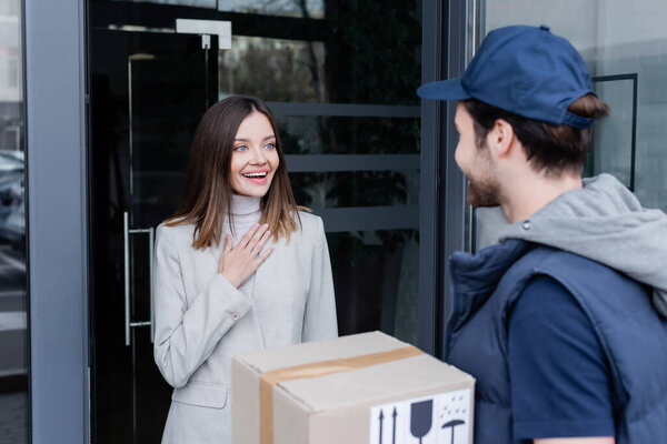 Excited woman looking at blurred courier near door of building outdoors 
