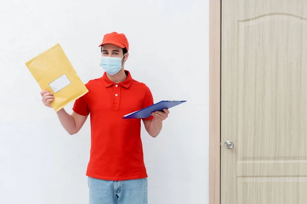 Courier Medical Mask Holding Parcel Clipboard Door Hallway — стоковое фото