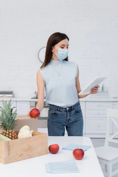 Woman Medical Mask Holding Apple Boxes Using Digital Tablet Kitchen — Stok Foto