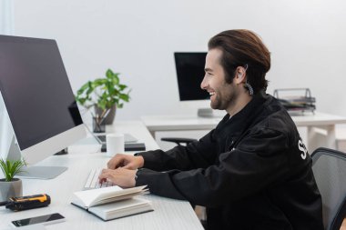Gülümseyen güvenlik görevlisinin defter ve telsizin yanında bilgisayarda yazışının yan görüntüsü