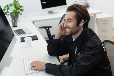 Kulaklıklı genç güvenlik görevlisi iş yerinde bilgisayar monitörünün yanında gülümsüyor.