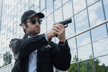 security man in black uniform and sunglasses holding gun while looking away on urban street clipart
