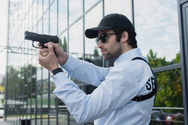 young guard in cap and sunglasses holding gun outdoors clipart