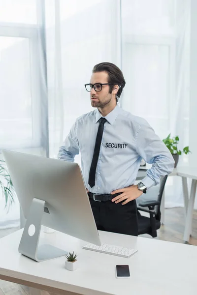 serious security man standing with hands on hips near computer monitor