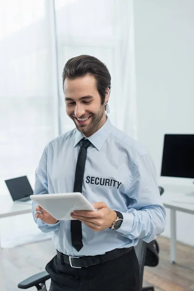 happy security man looking at digital tablet near computers on blurred background