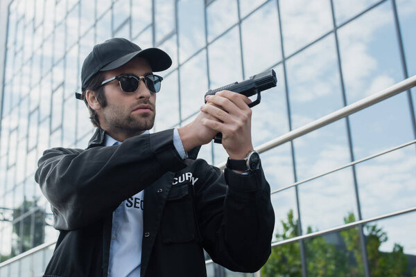 security man in black uniform and sunglasses holding gun while looking away on urban street