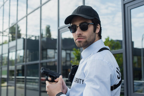 security man in black cap and sunglasses holding gun outdoors