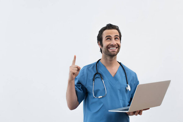happy doctor with laptop looking up and pointing with finger isolated on grey