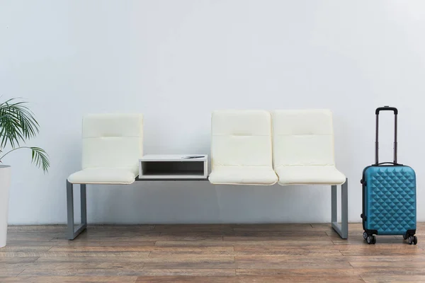 stock image white seats and blue travel bag near grey wall in departure lounge