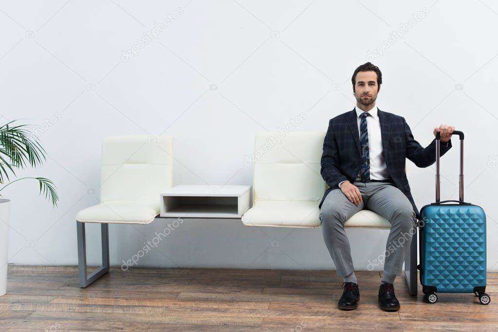 traveler waiting in departure lounge near suitcase and looking at camera 