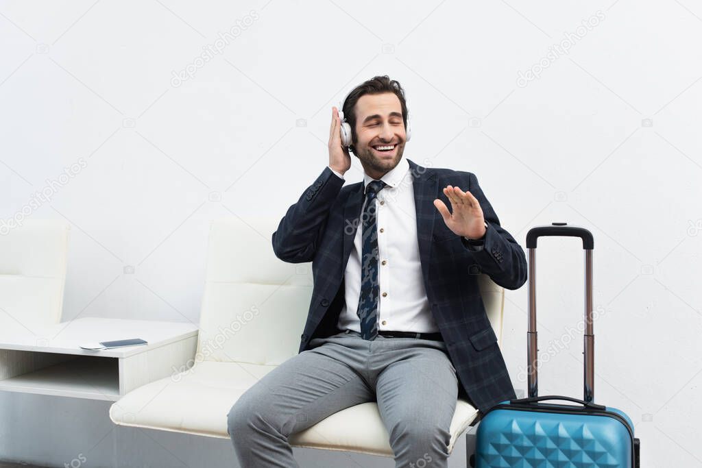 cheerful traveler sitting in departure lounge and listening music in headphones