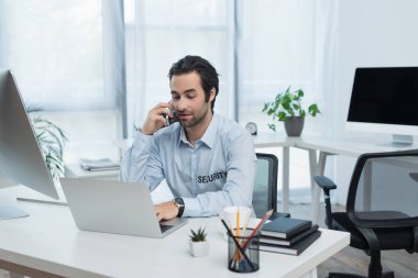 Ofiste akıllı telefonla konuşurken dizüstü bilgisayar kullanan pozitif güvenlik elemanı