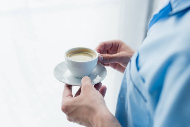Elinde kahve fincanı olan pijamalı bulanık adamın kısmi görüntüsü.