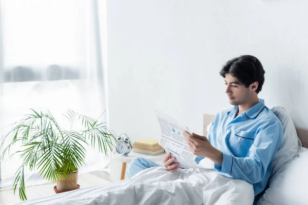 Jovem Pijama Azul Ler Jornal Perto Despertador Vintage Mesa Cabeceira — Fotografia de Stock