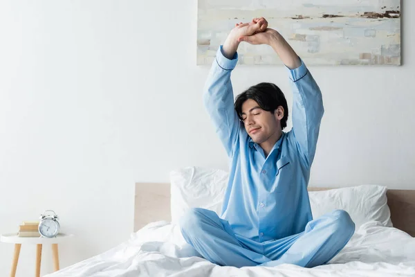 Smiling Man Blue Pajamas Stretching Arms Bed While Sitting Crossed — Stock Photo, Image