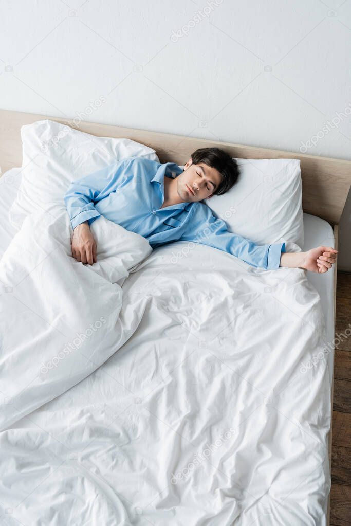 high angle view of young man in blue pajamas sleeping on white bedding