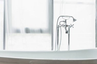 metal faucet with shower head, white bathtub near white curtain in bathroom clipart