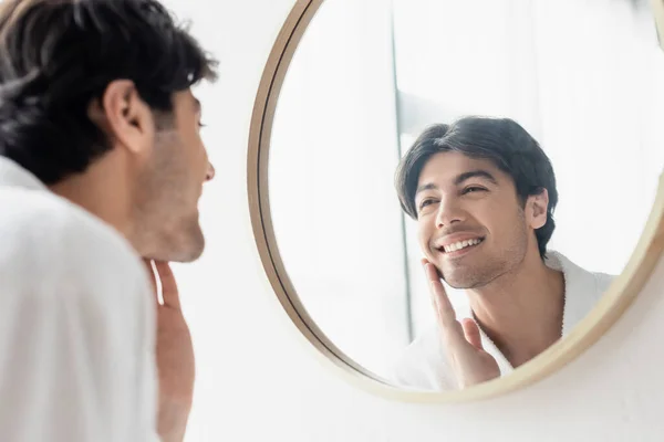 happy man looking in mirror and touching face in bathroom