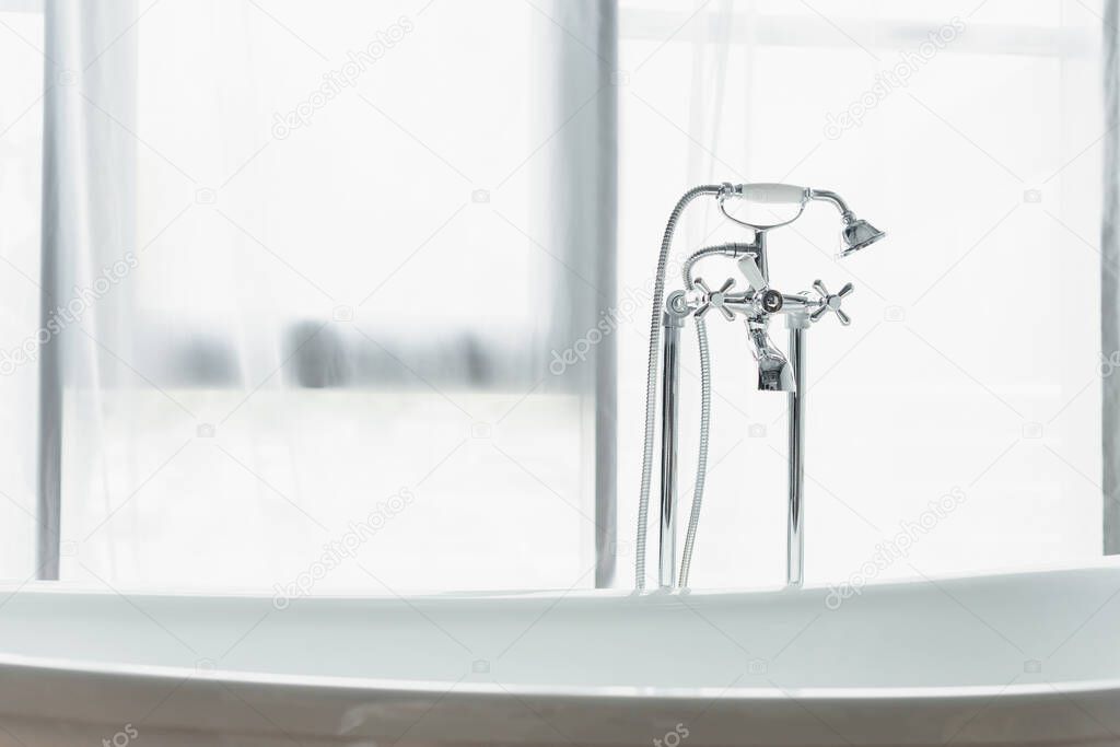 metal faucet with shower head, white bathtub near white curtain in bathroom