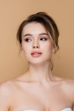 Genç ve güzel bir kadın, çıplak omuzlarıyla bej rengi bir elbiseye bakıyor.