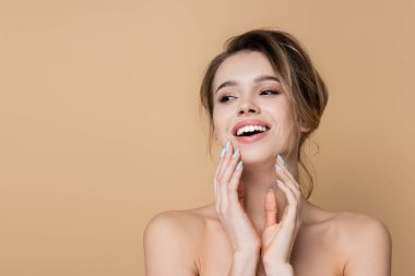 Doğal makyajlı, çıplak omuzları olan neşeli bir kadın. Bej rengi bir elbiseyle yüzünü çevirerek gülümsüyor.